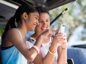two young girls one holding a mobile phone whilst other points to the screen
